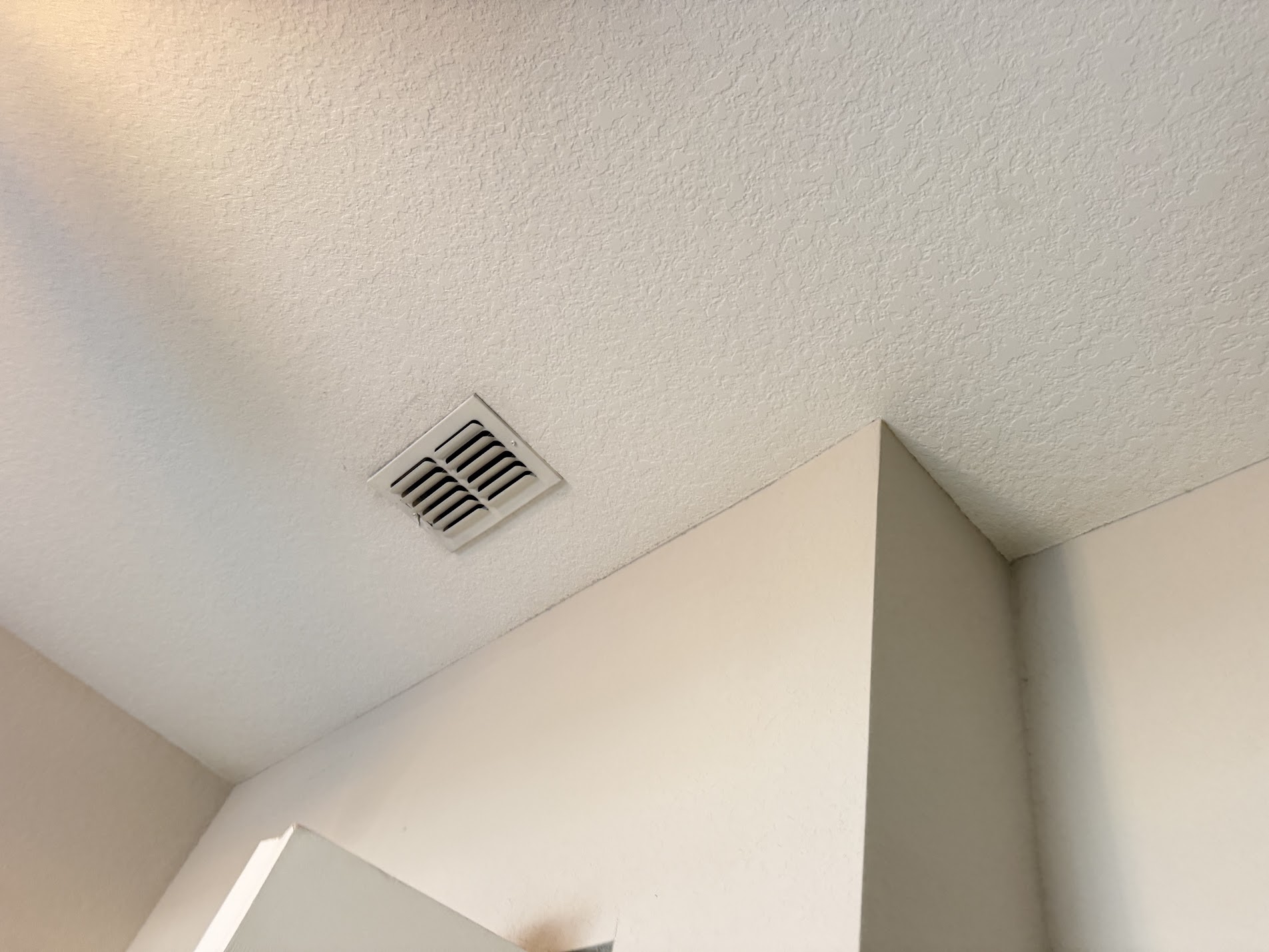 Clean ceiling and wall corner with a return grille, after repainting